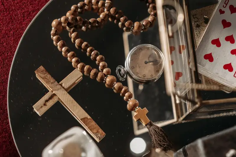 Close-up of vintage items including a pocket watch, rosary, cross, and playing cards on a mirror.